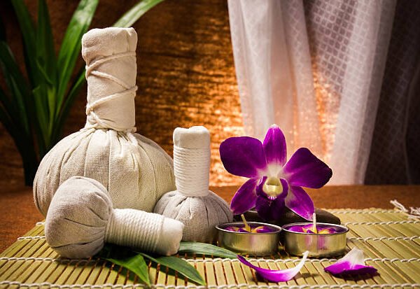 Spa herbal compressing ball with candles and orchid on brown background.